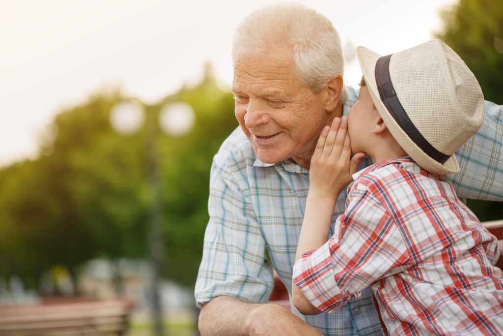 Young boy whispering into his grandfather’s ear.